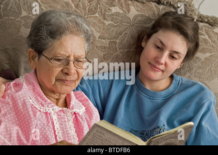 Head and shoulders of college student granddaughter and her grandmother reading book together on couch. Stock Photo