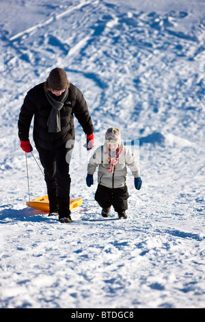 Mother and daughter walking up the sled hill after sleding down it during Winter, Anchorage, Southcentral Alaska Stock Photo