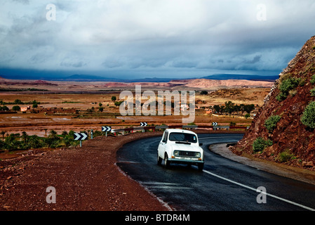 Old car on a narrow winding tar road with storm clouds over a plain Stock Photo