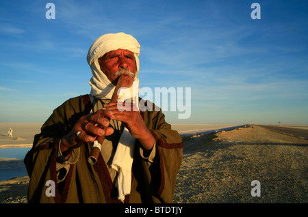 Elderly Berber man playing the flute next to the salt lake of Chott el-Jerrid Stock Photo