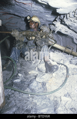 Drilling in an underground gold mine showing high pressure hoses and cramped working conditions. Stock Photo