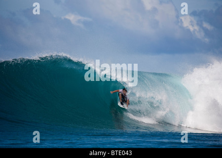 Man kneeling on his surf board about to be caught up in a breaking wave Stock Photo