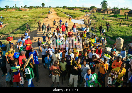 A large group of local villagers, many with bowls of fresh produce gathered in the road of a rural village Stock Photo