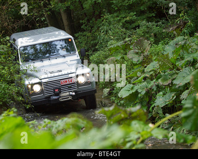 Silver Land Rover Defender driving through a creek at the Domaine d'Arthey estate in Belgium Stock Photo