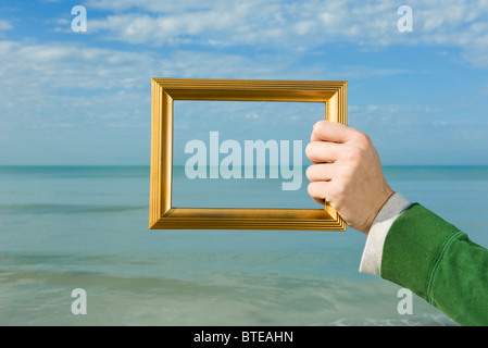 Person holding picture frame in front of ocean Stock Photo