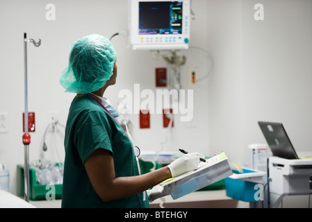 Nurse checking medical equipment monitor, recording data in medical chart Stock Photo