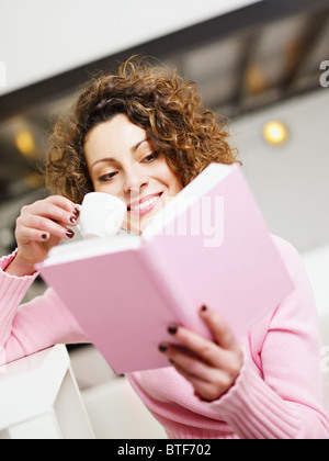 woman reading book at home and drinking coffee. Stock Photo