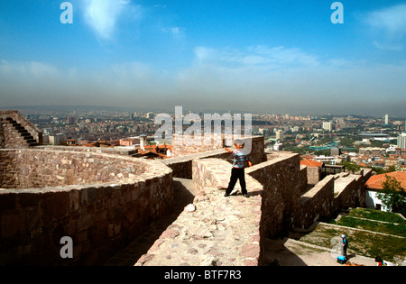 Young boy playing on the walls at the top of Ankara castle, Turkey with the capital city in the background below a pall of smog Stock Photo