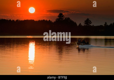 A fishing boat races across a calm lake at sunset, Minnesota. Stock Photo