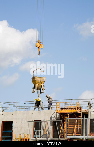 Construction workers guiding bucket suspended by crane to deposit concrete on building under construction Stock Photo