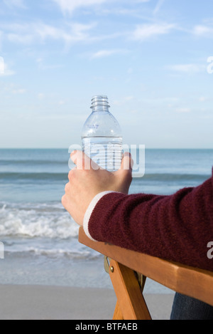 Person sitting relaxing at the beach, water bottle in hand Stock Photo