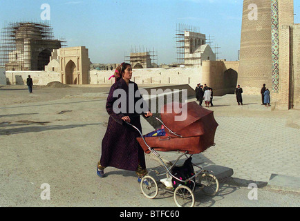 WOMAN PUSHING PRAM WALKING PAST THE KALYAN MOSQUE BEING RENOVATED IN BUKHARA, UZBEKISTAN Stock Photo