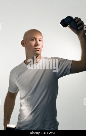 Bald man (20-25) in a white tee shirt and white background holding wireless camera flashes. Stock Photo