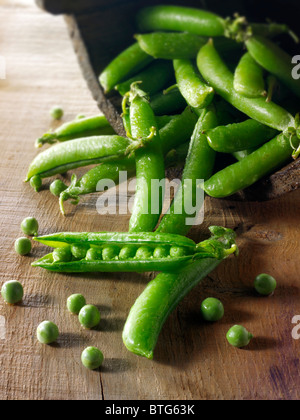 Food still life of fresh picked garden peas and pea in pods  on a rustic table in a kitchen being prepared Stock Photo