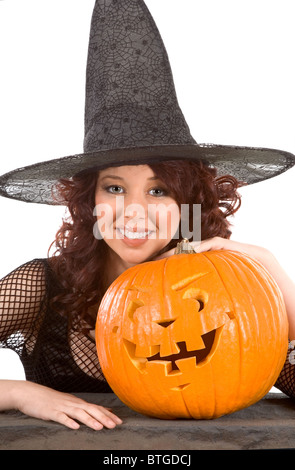 Portrait of Hispanic teenager girl in black Halloween hat and fishnet dress with carved  (Jack O' Lantern) (focus on pumpkin) Stock Photo