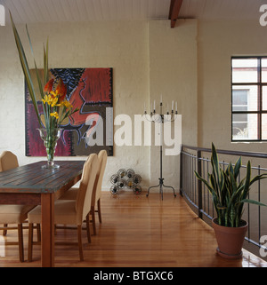 Large abstract painting on wall of modern dining room with tall-back chairs and old wood table and wooden flooring Stock Photo