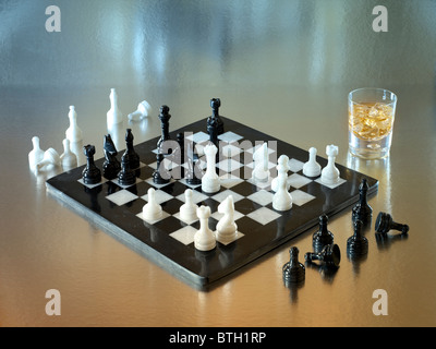A black and white chess set made of marble with glass of whiskey at the side Stock Photo