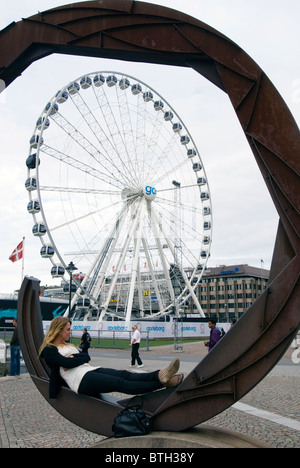 The Ferris Wheel on the waterfront in Gothenburg Sweden framed by a  woman relaxing in a modern steel sculpture Stock Photo