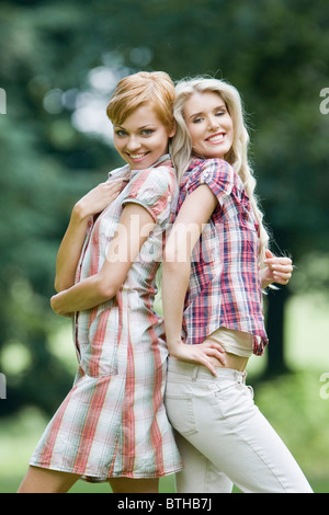 Two girlfriends, sisters, blonde in white festive dresses, look into