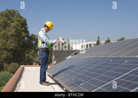 Maintenance worker stands with solar array on rooftop, Los Angeles, California Stock Photo