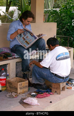 Young man reading a newspaper while getting a shoe shine in Santa Rosa de Copan, Honduras Stock Photo