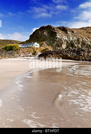 View from the beach and surf towards the white cafe hut on Kynance Cove beach, Cornwall Stock Photo