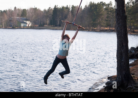 Young girl swinging on the bungee around the tree by the lake Stock Photo