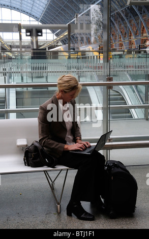 Portrait of a business woman sitting on a seat using a laptop computer in a railway station Stock Photo