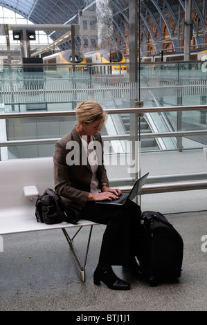 Portrait of a business woman sitting on a seat using a laptop computer in a railway station Stock Photo