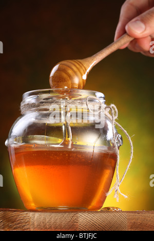 Hand holds drizzler. Sweet honey pouring from drizzler into the pot. Stock Photo