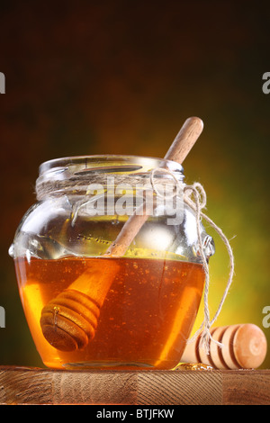 Sweet honey pouring from drizzler into the pot. Pot is on wooden table. Stock Photo