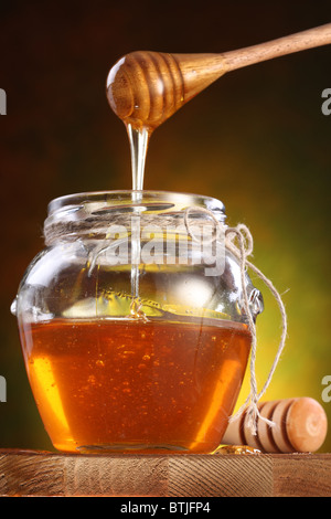 Sweet honey pouring from drizzler into the pot. Pot is on wooden table. Stock Photo