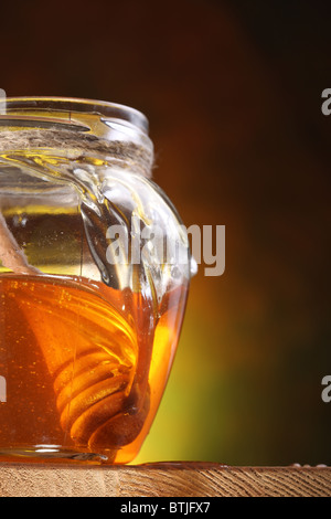 Pot of honey and wooden in it. Object is on wooden table. Stock Photo