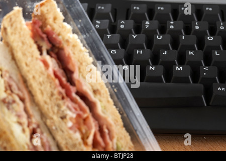 takeaway triple sandwiches in carton next to computer keyboard at lunchtime Stock Photo