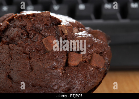 double choc chip chocolate muffin in front of computer keyboard at lunchtime Stock Photo