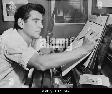 Leonard Bernstein (1918-1990), seated at piano, making annotations to musical score IN 1955. Bernstein composed score for two Broadway musicals, CANDIDE (1956), and WEST SIDE STORY (1957). Stock Photo