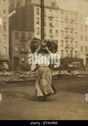 Italian woman carrying heavy bundle of clothing on her head Near Astor Place, New York City. She will sew the garments at home for low wages. February 1912 photograph by Lewis Hine. Stock Photo