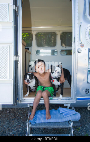 boy sitting in door of camper with dogs Stock Photo
