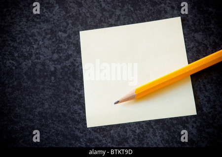 Yellow sticky note with a pencil against a dark marble background Stock Photo