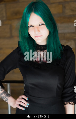 A young goth woman with green hair wearing a green dress and standing in a fire escape. Stock Photo