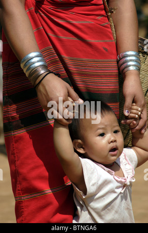 A Karen Paduang longneck refugee woman is helping her baby girl learn to walk at a refugee camp in Thailand. Stock Photo