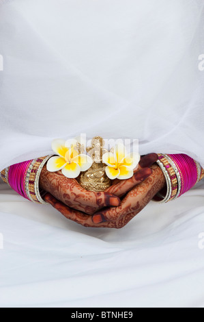 Indian girl wearing white silk sari with henna hands holding a Frangipani flower and a statue of Ganesha. India Stock Photo