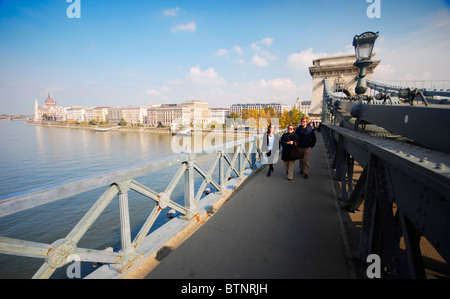 People crossing the Danube river on the famous Chain Bridge in Budapest, Hungary. In the background: The parliament building. Stock Photo