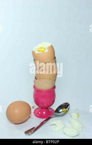 boiled egg on stack of empty egg shells in pink egg cup with spoon and  whole boiled egg Stock Photo