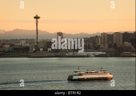 A beautiful sunrise illuminates the Space Needle and a ferry boat brings commuters into downtown Seattle, Washington, USA.