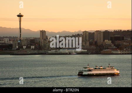 A beautiful sunrise illuminates the Space Needle and a ferry boat brings commuters into downtown Seattle, Washington, USA.