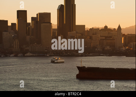 At dawn on Elliott Bay, Seattle, Washington, a ferry makes it's way to the downtown waterfront passing a container ship. Stock Photo