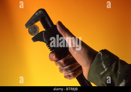 conceptual image of mechanic with oily hand holding adjustable spanner clamping two pound coin Stock Photo