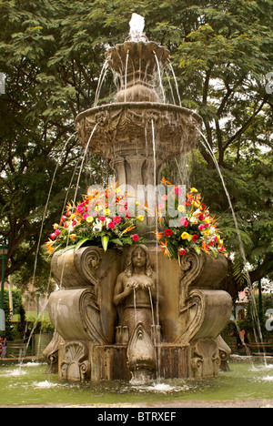 Flower bedecked fountain in the Parque Central, Antigua, Guatemala. Antigua is a UNESCO World heritage site. Stock Photo