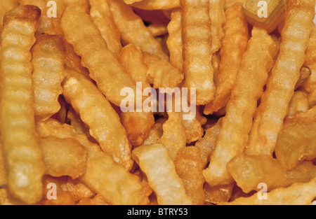 Close-up of a pile of golden fried crinkle cut French Fries that have been deep fried in oil. Stock Photo